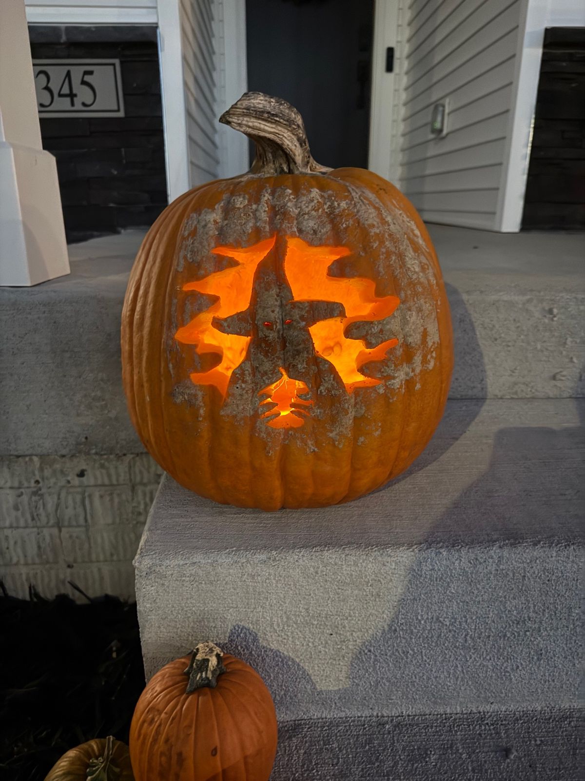 A lit jack-o'-lantern carved as a witch, sitting on the porch steps at 345 Cormorant